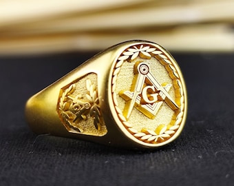 Può includere: Un anello d'oro con un simbolo massonico inciso sulla parte superiore. Il simbolo è un compasso e una squadra con una 'G' al centro.