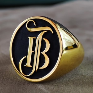 This close-up image presents a custom monogram signet ring designed with engraved initials on a smooth, polished face. The ring is available in Silver, Gold Plated, and 14k Gold variations, giving shoppers multiple material choices. The engraving is crisp and symmetrical, showing the precision of the craftsmanship. The lighting captures the reflective surface of the ring, emphasizing its luxurious appearance and suitability as a personalized Christmas gift for him or her.