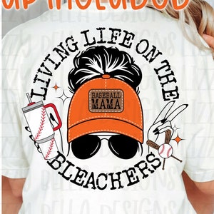 May include: A white t-shirt mockup with a graphic design featuring a woman with a baseball cap that says "Baseball Mama" and sunglasses. The graphic also includes a baseball bat, a drink, and the text "Living Life on the Bleachers".