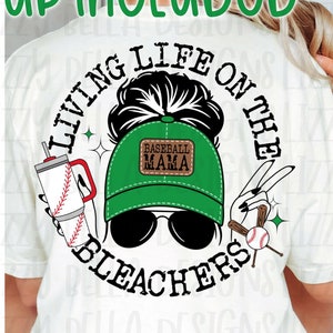 May include: A white t-shirt mockup with a graphic design featuring a woman with a messy bun wearing a green baseball cap with the text "Baseball Mama" and sunglasses. The graphic also includes a baseball bat, a baseball, and a drink with a straw. The text "Living Life on the Bleachers" is written in a circle around the woman's head.