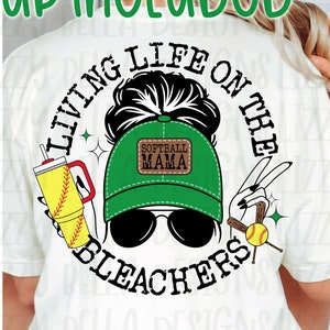 May include: A white t-shirt mockup with a graphic design featuring a woman with a bun, sunglasses, and a green baseball cap with the text "Softball Mama". The graphic is surrounded by a circle with the text "Living Life on the Bleachers".