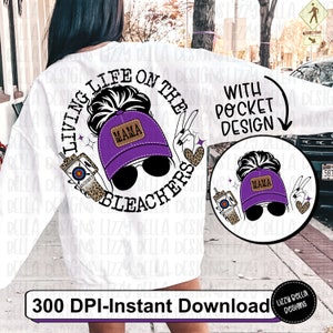 May include: A white sweatshirt with a purple and black graphic design that says "Living Life on the Bleachers" with a woman wearing a purple baseball cap that says "Mama" on it. The graphic also includes a drink with a target on it and a heart with leopard print. The text "With Pocket Design" is also included on the sweatshirt.