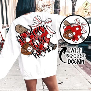 May include: White sweatshirt with a baseball-themed graphic. The design features a red home plate with white polka dots, a baseball bat, a baseball glove, and a baseball. The text "No Place Like Home" is written in a script font.