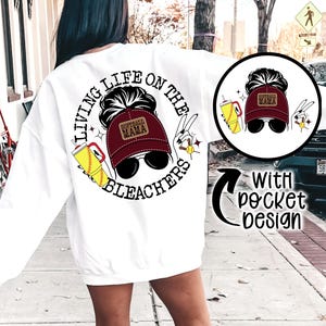May include: White sweatshirt with a circular graphic on the back featuring a woman in a maroon baseball cap and sunglasses, with the text "Living Life on the Bleachers." A smaller graphic is on the front, with the words "With pocket design."