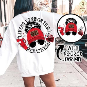 May include: White sweatshirt with a graphic design featuring a woman wearing a red "Cheer Mama" hat and sunglasses. The design includes the text "Living Life on the Bleachers" and a small pocket design.