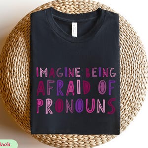 May include: Black t-shirt with the text "Imagine being afraid of pronouns" in pink, purple, and red lettering.