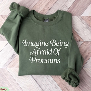 May include: A green sweatshirt with the text "Imagine Being Afraid Of Pronouns" printed in white.