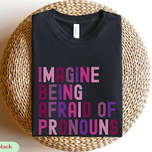 May include: Black t-shirt with the text "Imagine being afraid of pronouns" in pink, purple, and red letters.