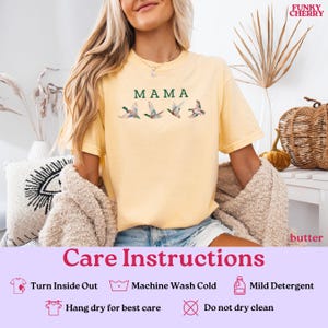 Peut inclure: T-shirt jaune beurre avec le mot "MAMA" en vert et une illustration &agrave; l'aquarelle de quatre canards en vol. Le t-shirt a des manches courtes et un col rond. Le logo Funky Cherry est dans le coin sup&eacute;rieur droit.