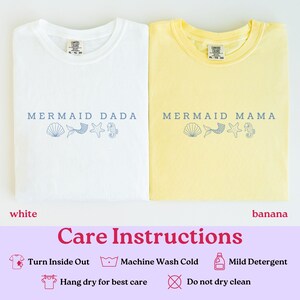 Puede incluir: Se muestran dos camisetas, una blanca y otra amarilla pl&aacute;tano. La camiseta blanca dice "MERMAID DADA" y la camiseta amarilla dice "MERMAID MAMA" en texto azul. Ambas camisetas tienen gr&aacute;ficos de conchas marinas, cola de sirena, estrella de mar e hipocampo. Tambi&eacute;n se muestran instrucciones de cuidado.