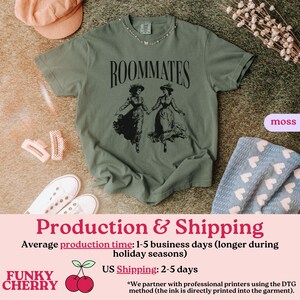 May include: A green t-shirt with the text "ROOMMATES" printed in black. The shirt features a black and white illustration of two women in vintage dresses.