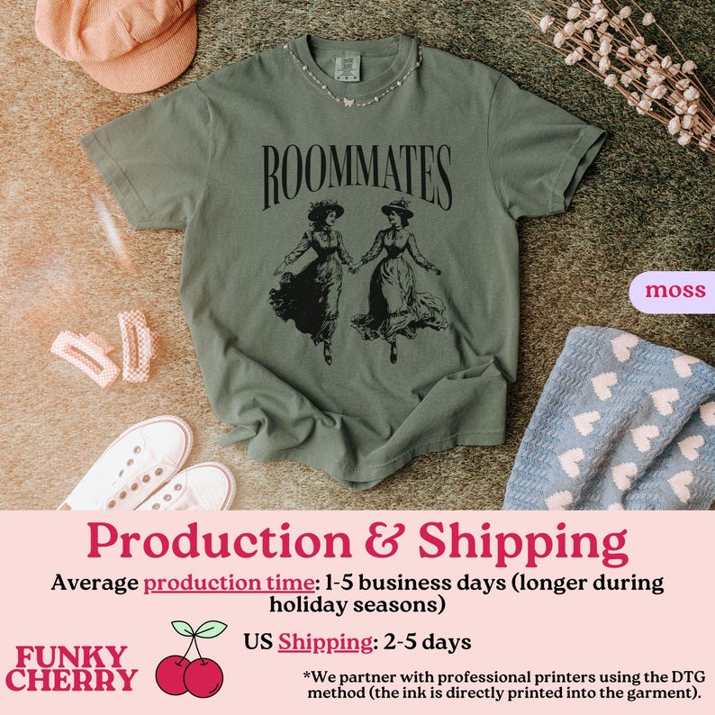 May include: A green t-shirt with the text "ROOMMATES" printed in black. The shirt features a black and white illustration of two women in vintage dresses.