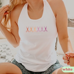 May include: White tank top with a row of five ombre scissors printed on the front. The scissors are in shades of orange, pink, and purple.