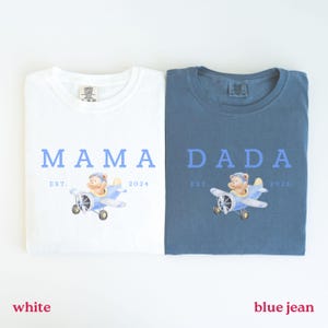 Puede incluir: Dos camisetas, una blanca y otra azul, con las palabras "MAMA" y "DADA" en azul. Cada camiseta presenta una ilustración en acuarela de un oso de peluche en un avión azul, con "EST. 2024" debajo. La camiseta blanca está etiquetada como "white" y la camiseta azul como "blue jean".