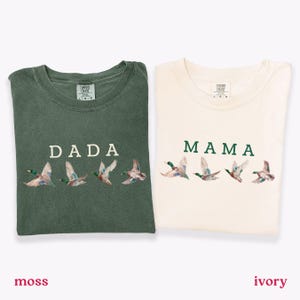Peut inclure: Deux t-shirts pli&eacute;s, l'un vert mousse et l'autre ivoire. Le t-shirt vert mousse porte l'inscription "DADA" avec des canards brod&eacute;s. Le t-shirt ivoire porte l'inscription "MAMA" avec des canards brod&eacute;s.