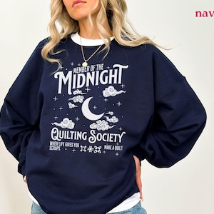 Puede incluir: Sudadera azul marino con texto blanco. El diseño presenta las palabras "MEMBER OF THE MIDNIGHT QUILTING SOCIETY", una luna creciente, nubes y estrellas. También incluye el texto "WHEN LIFE GIVES YOU SCRAPS MAKE A QUILT".