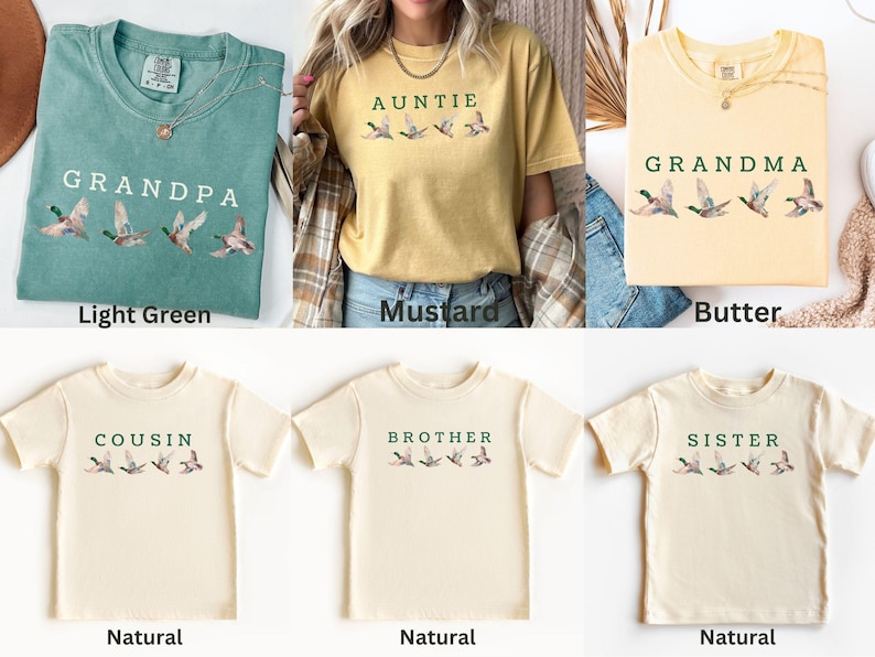 Peut inclure: Plusieurs t-shirts de couleurs vert clair, moutarde et naturel. Chaque t-shirt affiche un titre familial tel que "Grand-p&egrave;re" ou "Tante" en vert, accompagn&eacute; d'un motif de canard.