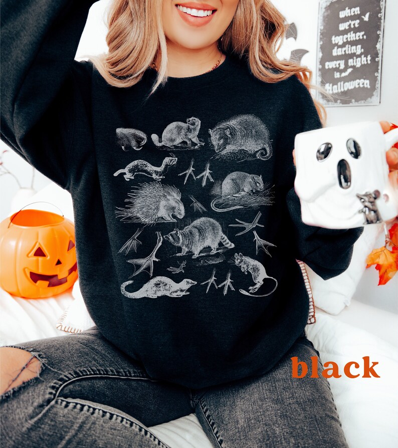 May include: Black sweatshirt featuring a white graphic print of various animals, including a raccoon, opossum, and porcupine. The text "When we're together, darling, every night is Halloween" is visible in the background.