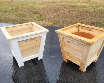 Könnte beinhalten: Zwei Holzpflanzgefäße. Eines ist weiß lackiert mit Naturholzlatten, das andere ist Naturholz mit einem Terrakottatopf im Inneren. Beide sind quadratisch und haben ein schlichtes, modernes Design. Ideal für die Außendekoration.