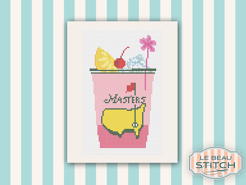 May include: A pink and yellow cross-stitch design of a cocktail glass with a lemon wedge, cherry, and a golf flag. The glass has the word "Masters" written on it.