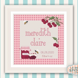 May include: Cross-stitch pattern featuring a pink and white gingham background with a jar of cherry jam, bees, and cherries. The text reads "meredith claire" and "06.28.2020 6lbs 4oz".