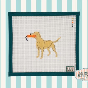 Puede incluir: Lienzo de punto de aguja con un Labrador Retriever amarillo sosteniendo un juguete naranja. El perro est&aacute; cosido sobre lienzo blanco, enmarcado por un borde verde oscuro. El dise&ntilde;o incluye el texto "LBS" y el logotipo "Le Beau Stitch".