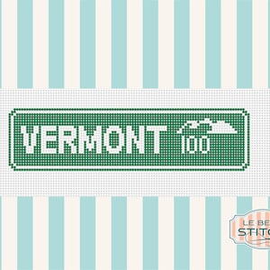 May include: A cross-stitch pattern featuring a rectangular green sign with white text that reads VERMONT 100 and a small white mountain graphic. The design is set against a background of vertical light blue and white stripes with a logo in the corner.