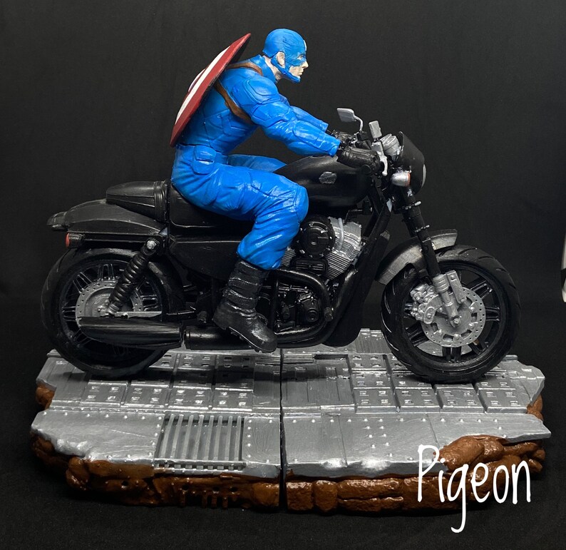 May include: A blue and red action figure of Captain America riding a black motorcycle with a silver base. The motorcycle has a silver exhaust pipe and a silver front wheel.