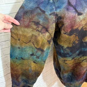 May include: A tie-dye sweatshirt in shades of blue, purple, gold, and brown. The garment has a unique, marbled effect, with the colors blending and swirling together. The sleeve is visible, showcasing the intricate dye pattern.