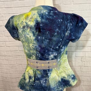 May include: A short-sleeved jacket with a tie-dye pattern in shades of blue, yellow, and purple. The jacket has a fitted waist with a decorative belt and a peplum hem. The fabric appears to be cotton or a similar material.