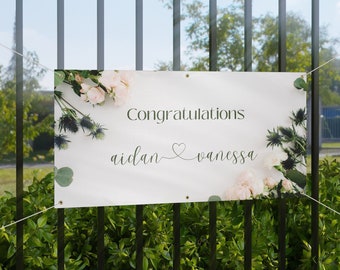 May include: White banner with floral design and the text "Congratulations Aidan ♥ Vanessa" printed in black.