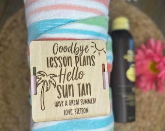 Könnte beinhalten: Ein gerolltes Strandtuch mit rosa, weißen, blauen und grünen Streifen. Ein Holzschild mit dem Text "Goodbye Lesson Plans Hello Sun Tan" ist angebracht. Eine Flasche Bräunungslotion ist im Hintergrund zu sehen.