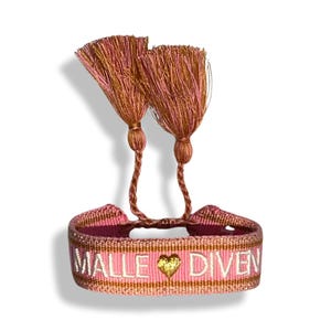 May include: Pink and gold woven bracelet with a heart and the text "MALLE DIVEN". The bracelet has two tassels.