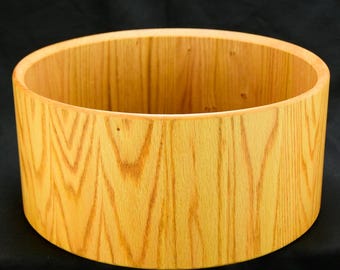 May include: A cylindrical wooden bowl with a light brown finish. The bowl has a smooth, rounded rim and a natural wood grain pattern. The interior and exterior are the same color. The bowl is likely handmade.