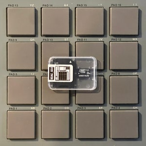 Może przedstawiać: Szary i czarny elektroniczny pad do produkcji muzyki z włożoną kartą SD oznaczoną jako "BDAC_SD2". Pad ma 16 przycisków oznaczonych literami i symbolami.