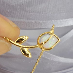May include: A gold rose necklace with a white opal gemstone in the center of the rose. The necklace has a delicate chain.