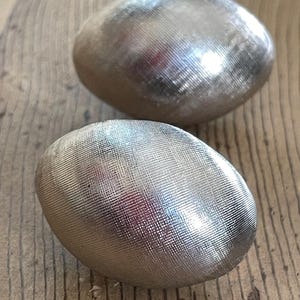 May include: Two silver, metallic, egg-shaped ornaments with a textured surface.