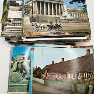 May include: A large collection of vintage postcards featuring various scenes including the Austrian Parliament building with a horse-drawn carriage, a sphinx statue on Memorial Boulevard in Winnipeg, and a brick house with a thatched roof.
