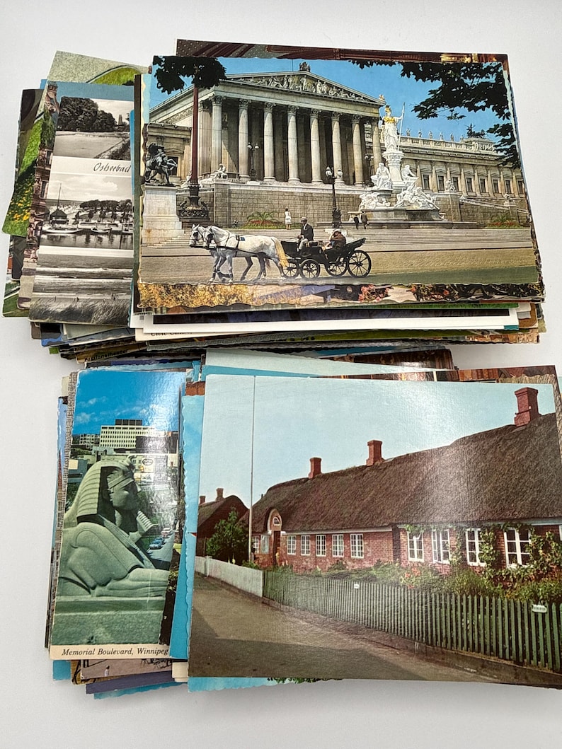 May include: A large collection of vintage postcards featuring various scenes including the Austrian Parliament building with a horse-drawn carriage, a sphinx statue on Memorial Boulevard in Winnipeg, and a brick house with a thatched roof.
