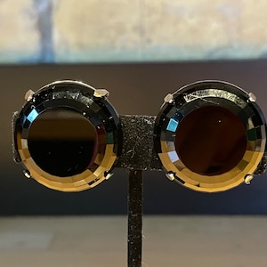 Puede incluir: Un par de pendientes de piedra preciosa negra con un diseño facetado. Los pendientes son redondos y tienen un engaste plateado.