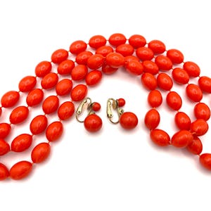 May include: A set of orange plastic bead jewelry, including a necklace and clip-on earrings. The necklace is made of three strands of large, oval-shaped beads.