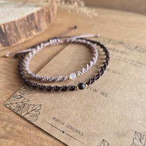 May include: Two macrame bracelets, one light brown and one dark brown, each with a central gemstone bead. The bracelets are displayed on a textured surface with a card that reads "MAGIA SZNURKA" and "FOR ME".