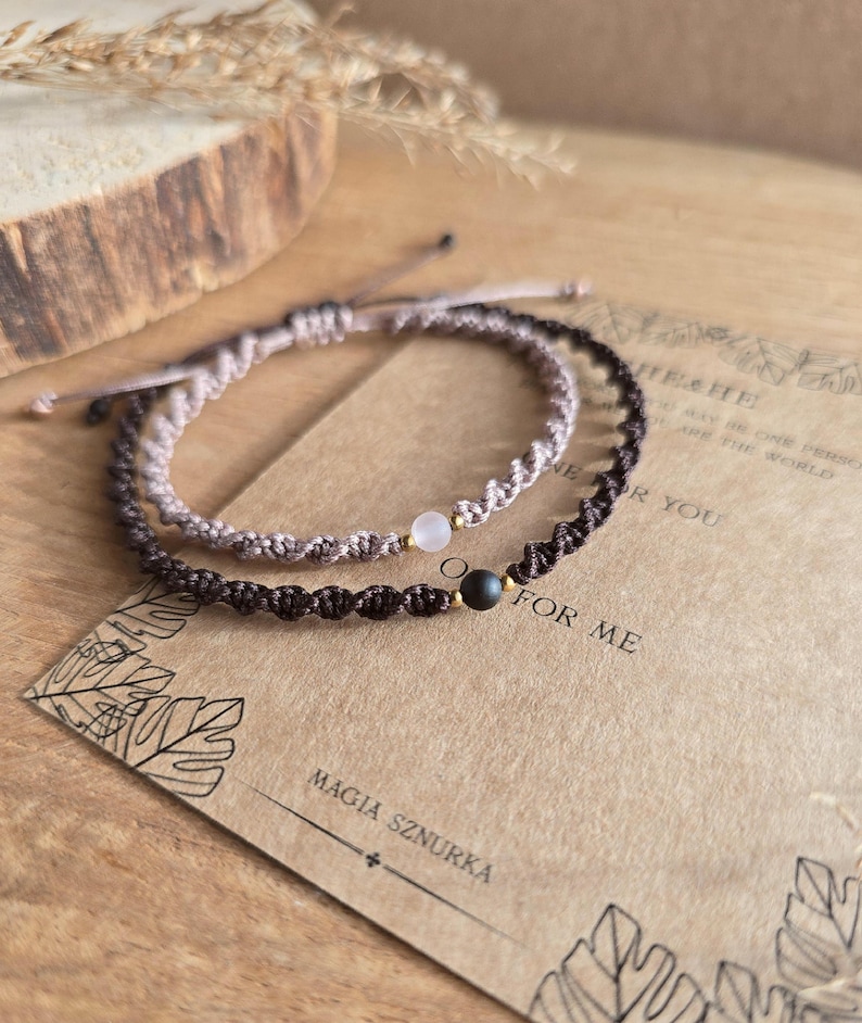 May include: Two macrame bracelets, one light brown and one dark brown, each with a central gemstone bead. The bracelets are displayed on a textured surface with a card that reads "MAGIA SZNURKA" and "FOR ME".