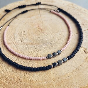 May include: Two beaded bracelets, one black and one pink, with silver square beads in the centre.