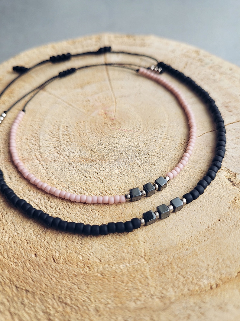 May include: Two beaded bracelets, one black and one pink, with silver square beads in the centre.