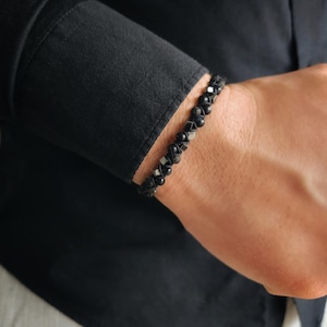 May include: A black beaded bracelet with silver accents. The bracelet is made of small, round beads and is worn on a person's wrist.