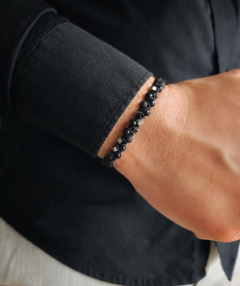 May include: A black beaded bracelet with silver accents. The bracelet is made of small, round beads and is worn on a person's wrist.
