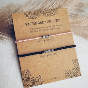May include: A set of two bracelets with a card that reads "Father & Daughter. To the world, you may be one person, but for me, you are the world. One for you. One for me." The bracelets are made of black and pink beads with silver metal accents.