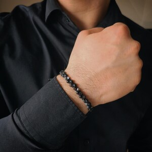May include: A black beaded bracelet with a silver clasp. The bracelet is made of small, round beads that are strung together on a black cord.