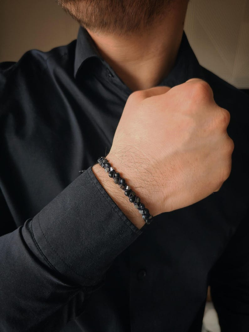 May include: A black beaded bracelet with a silver clasp. The bracelet is made of small, round beads that are strung together on a black cord.